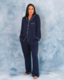 Woman wearing navy blue pajamas with white piping against a textured gray background