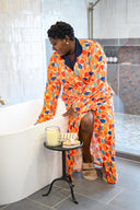 Woman in a colorful robe sitting by a bathtub with a candle and towel.